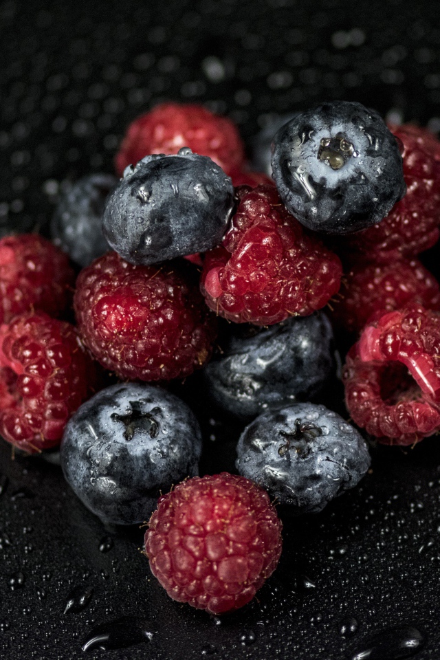 Мокрые ягоды черники и малины на черном фоне