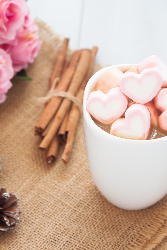 Чашка какао с маршмеллоу на столе с корицей, шишками и букетом розовых роз