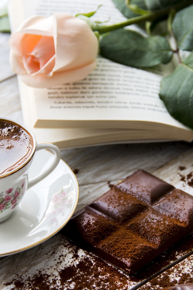Чашка кофе на столе с шоколадом, книгой и розой