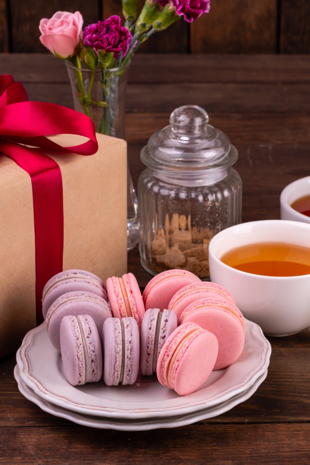 Подарок с красной лентой на столе с макарунами и чаем 