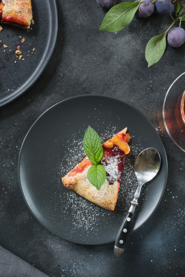 Кусок пирога с сахарной пудрой и абрикосами и сливами на столе с чаем 