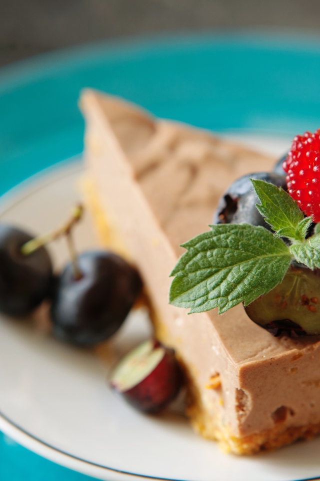 Кусок чизкейка на тарелке с ягодами черники и малиной