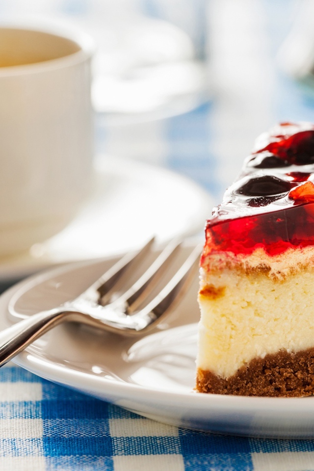 Кусок чизкейка с ягодами и желе на столе с чашкой кофе