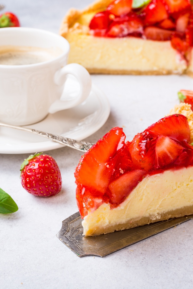 Кусок чизкейка с клубникой на столе с кофе