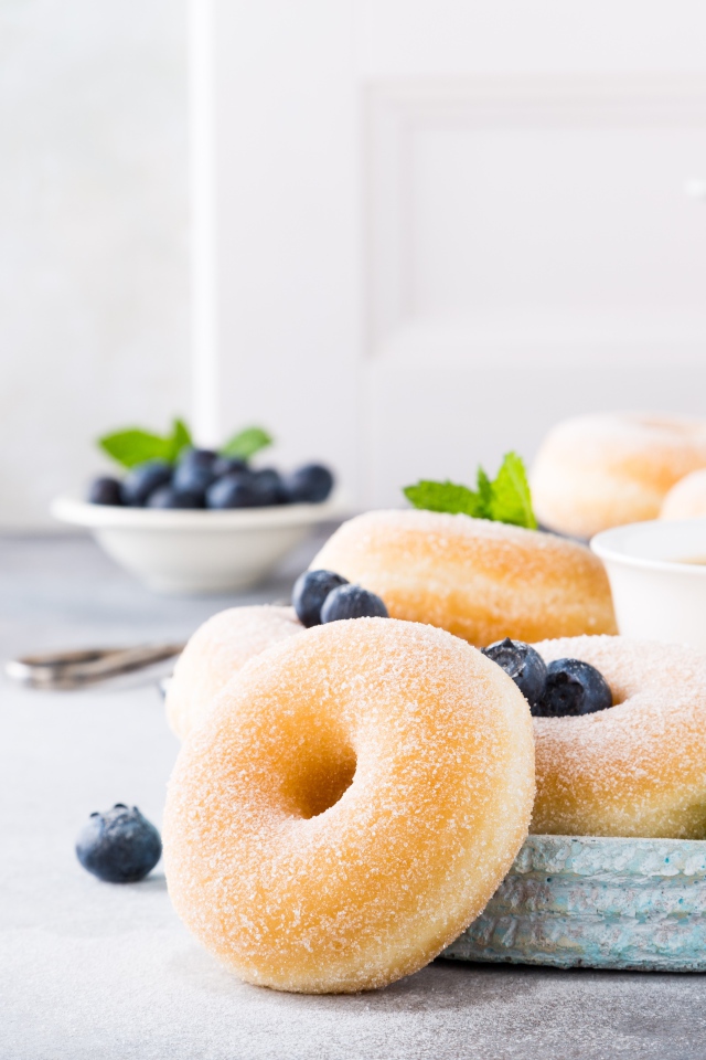 Аппетитные пончики с сахарной пудрой на столе с черникой