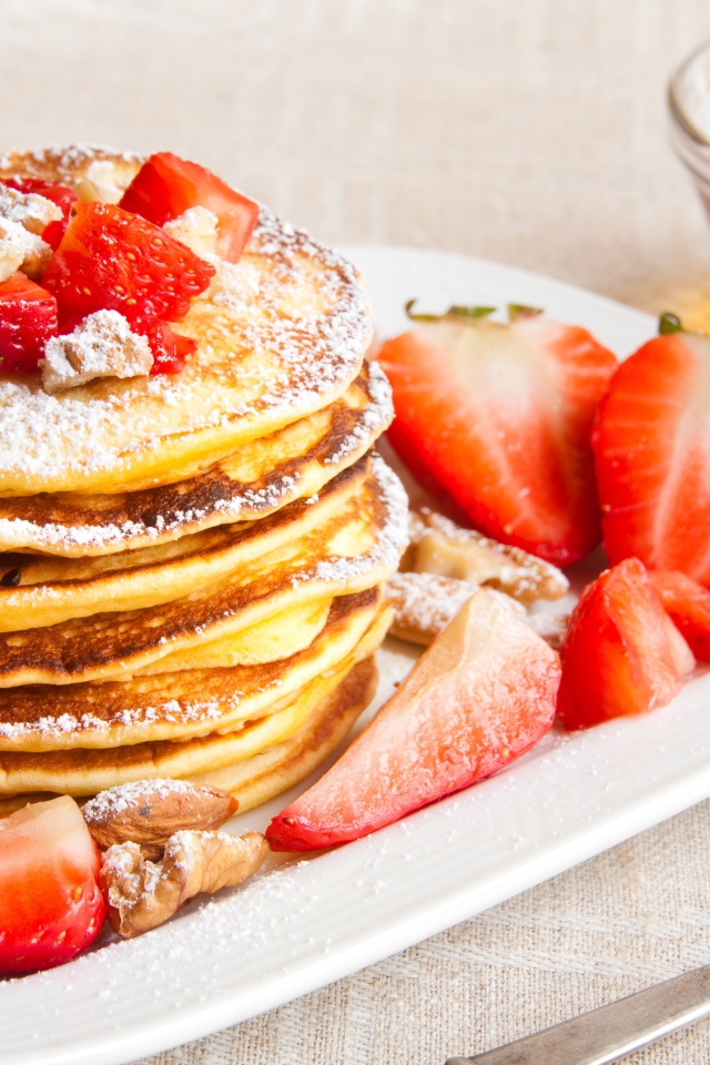 Appetizing sweet pancakes with icing sugar and strawberries