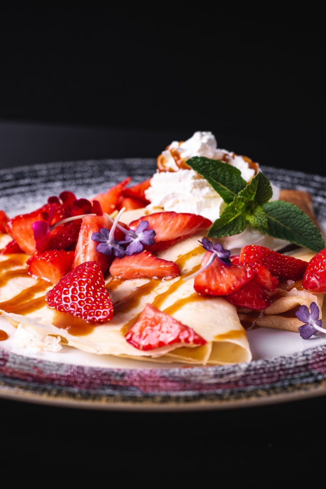 Аппетитные тонкие блинчики с клубникой на черном фоне