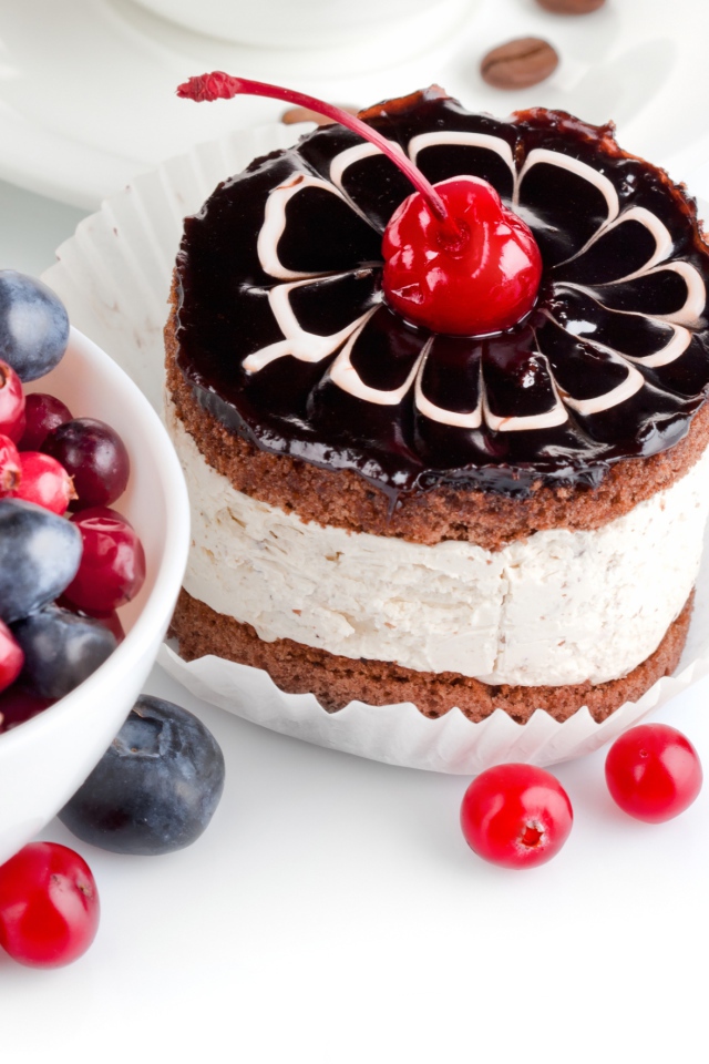 Пирожное с вишней на белом фоне с ягодами черники и клюквы