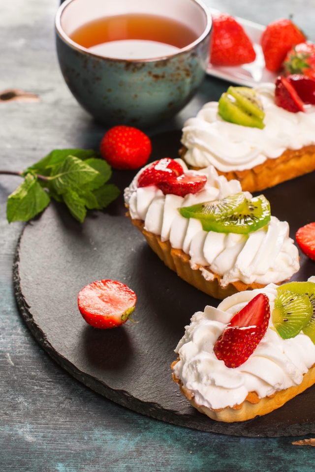 Пирожные с киви и клубникой на столе с чаем