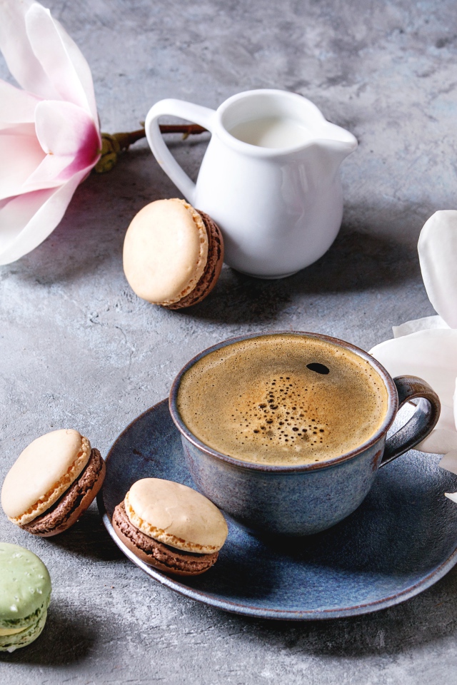 Кофе на столе с макарунами, молоком и цветами 