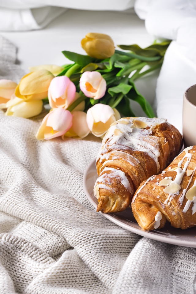 Круассаны на кровати с кофе и букетом тюльпанов