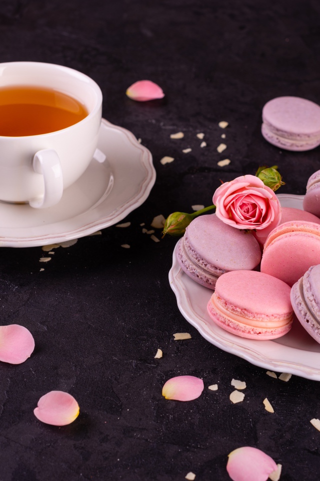 Нежный десерт макарон на столе с чашкой чая и розой