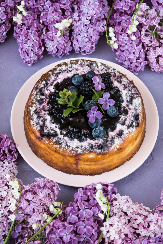 Аппетитный пирог с ягодами на столе с цветами сирени