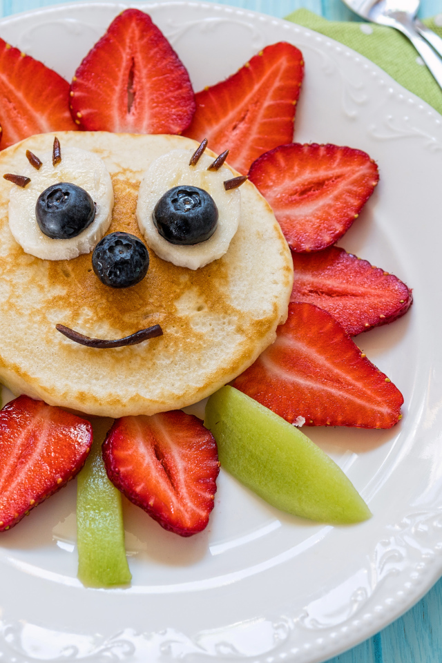 Цветок из клубники, оладьей и киви  на белой тарелке