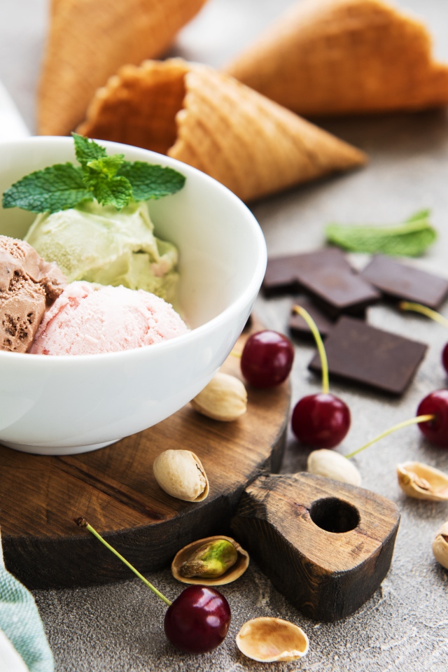 Шарики мороженого на столе вафельными рожками, черешней и фисташками