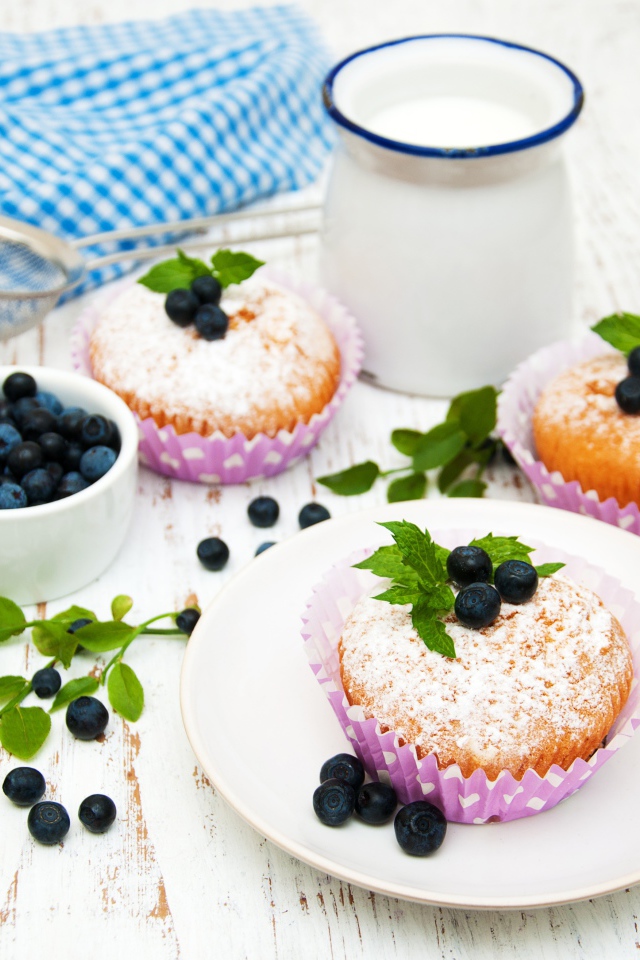 Кексы с сахарной пудрой на столе с молоком и черникой