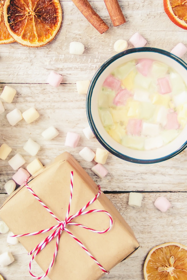 Кружка горячего напитка на столе с маршмеллоу, пряностями и подарком