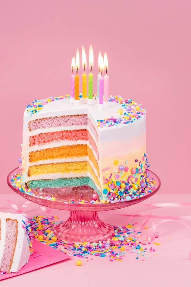 Разноцветный праздничный торт со свечами на розовом фоне