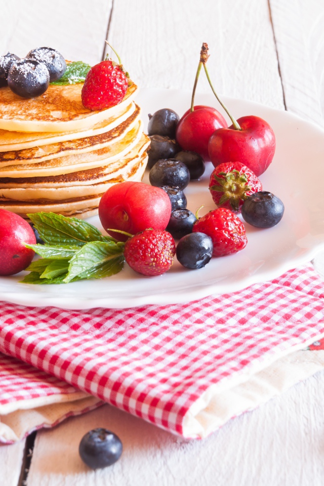 Оладья на белой тарелке с ягодами черники, черешни и клубники