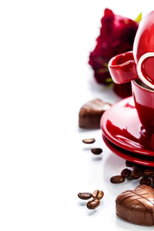 Красные чашки на белом фоне с шоколадными конфетами и кофейными зернами