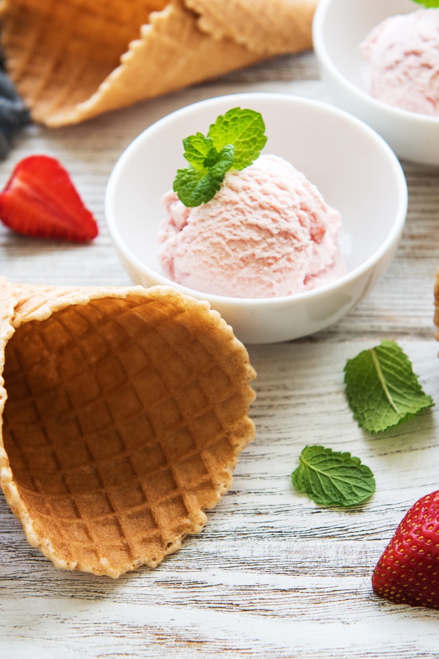 Клубничное мороженое на столе с рожками и клубникой