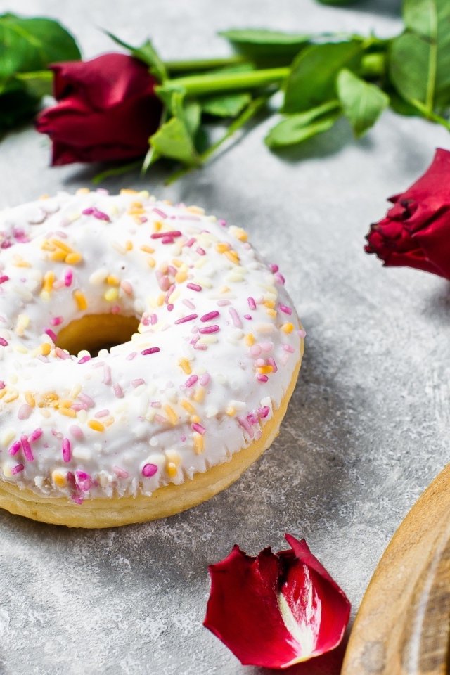 Сладкий пончик с глазурью на столе с красными розами