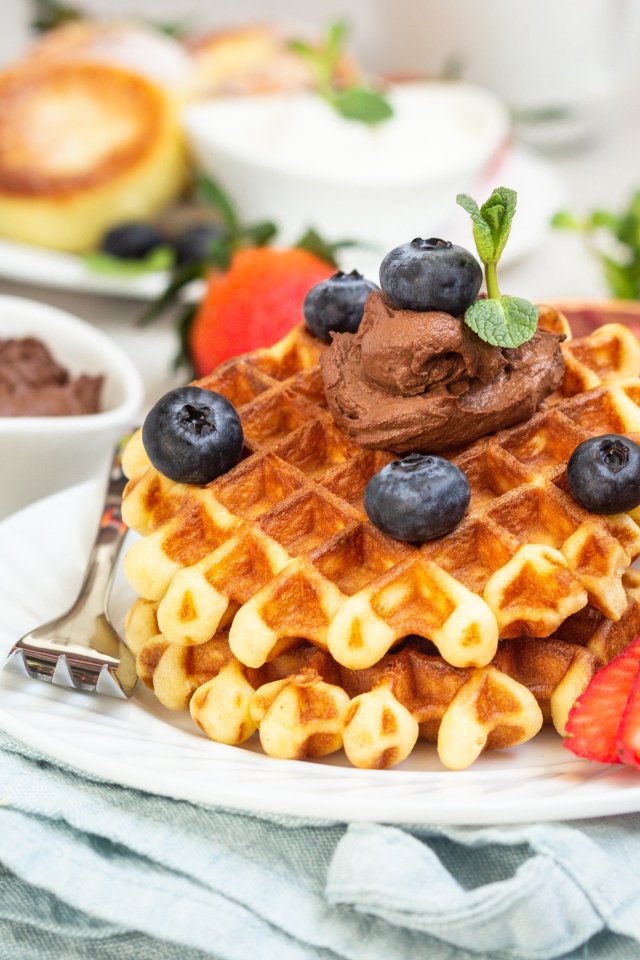 Сладкая вафля с шоколадом, ягодами черники и клубники на тарелке