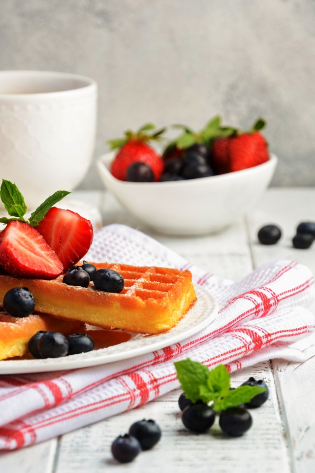 Сладкие вафли с ягодами черники и клубники на столе с медом и чаем