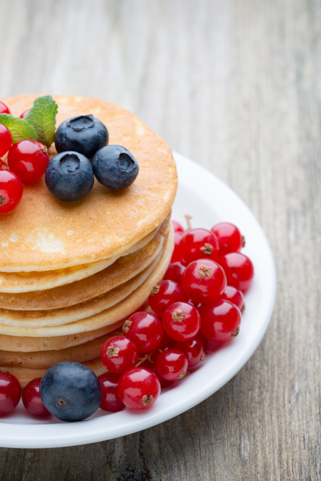 Вкусные оладьи на тарелке с ягодами красной смородины и черники