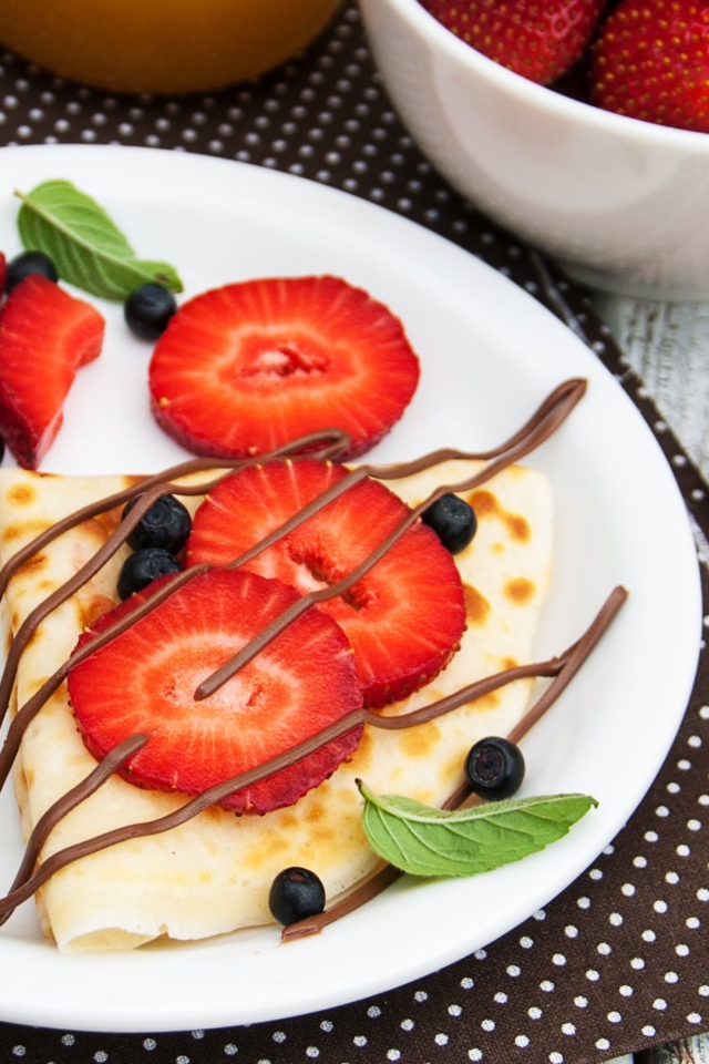 Тонкий блинчик на тарелке с шоколадом, ягодами клубники и черники