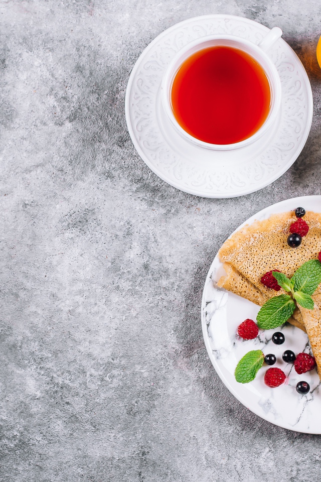 Тонкие блинчики на столе с ягодами, чаем и медом
