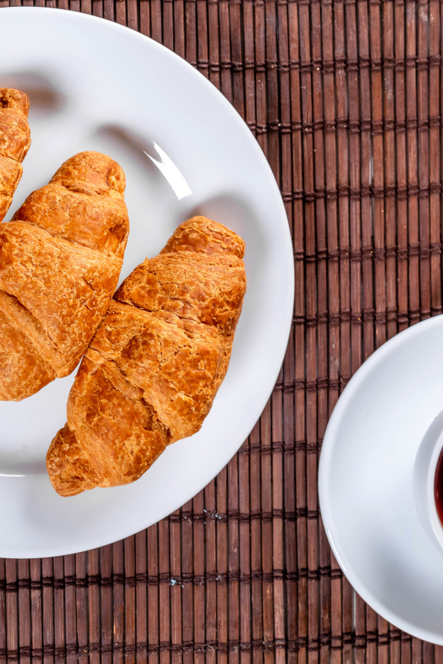 Три круассана на белой тарелке на столе с чаем