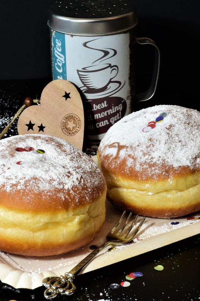 Два пышных пончика с сахарной пудрой на черном столе с кофе