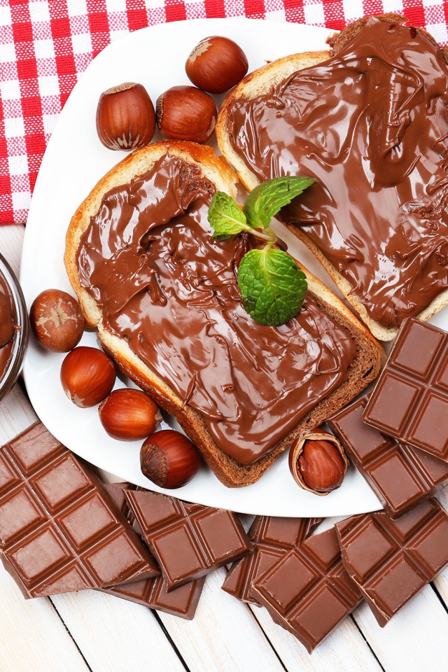 Два куска с шоколадной пастой на столе с шоколадом и орехами