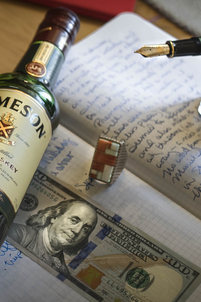 Бутылка виски лежит на тетради с чернильницей и купюрой