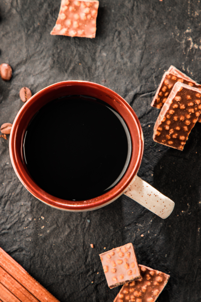 Чашка кофе на столе с кусочками шоколада и кофейными зернами