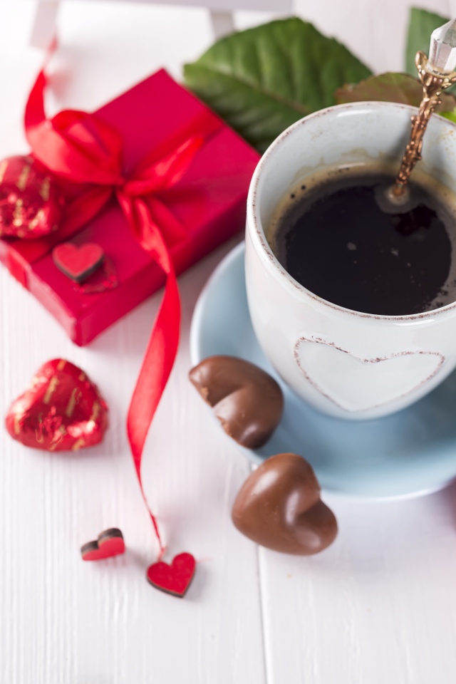 Чашка кофе на столе с шоколадными конфетами, подарком и красной розой