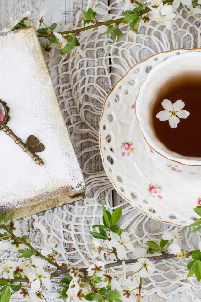 Чашка чая на столе с книгой и белыми цветами вишни 