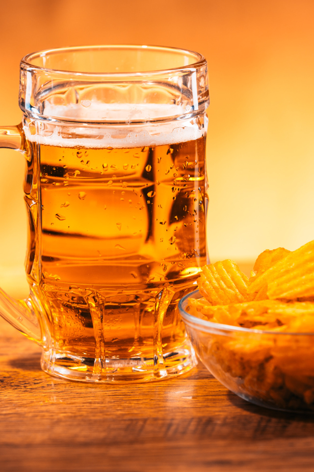 Бокал пива с тарелкой чипсов на столе 