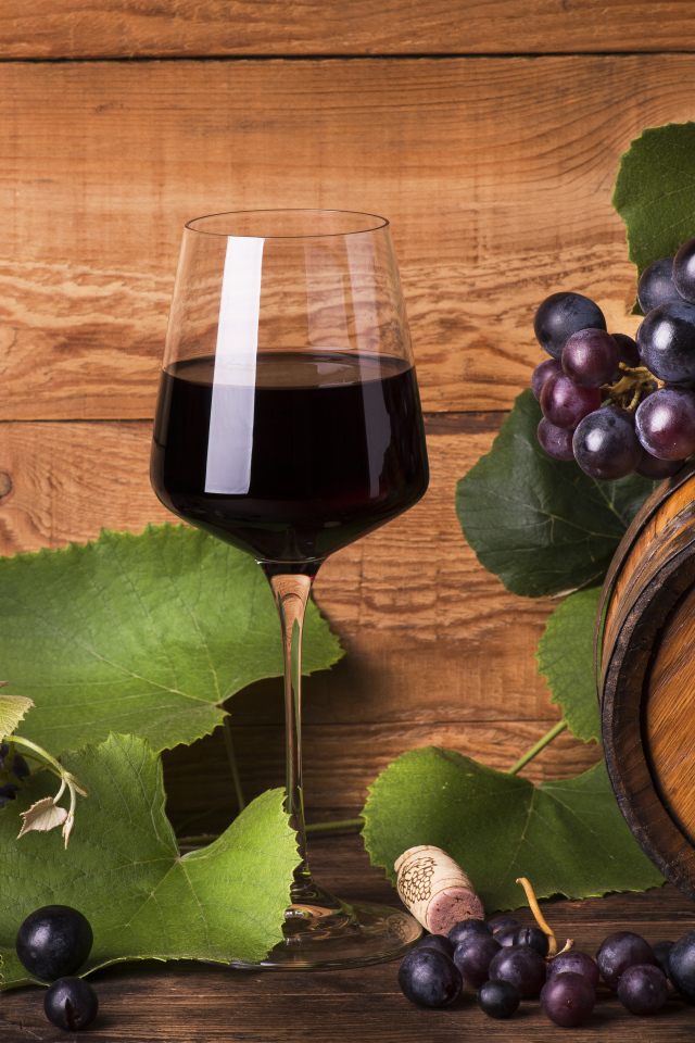 Бокал красного вина  на столе с виноградом и бочкой