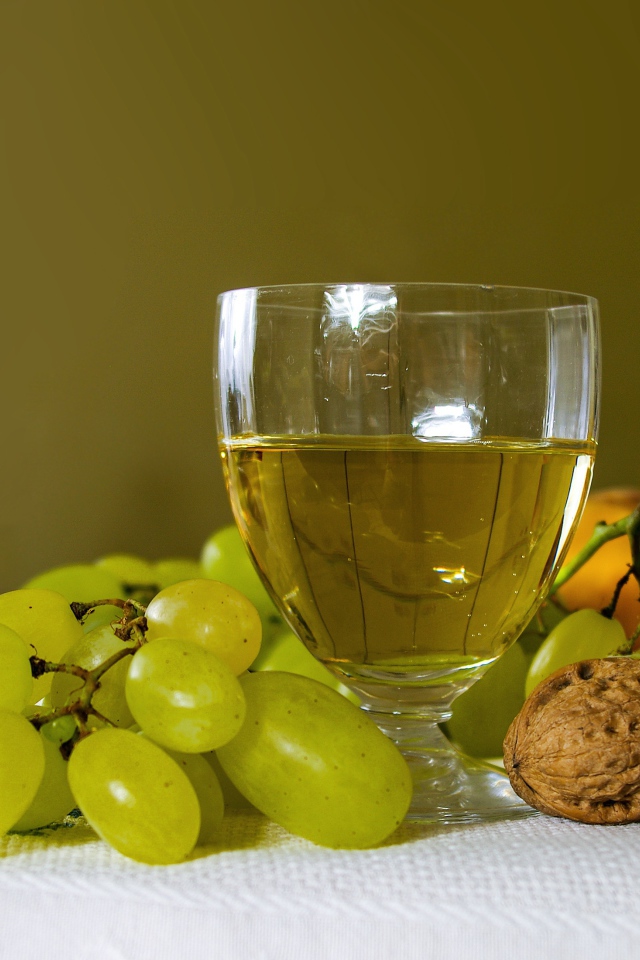 Бокал белого вина на столе с виноградом и орехами