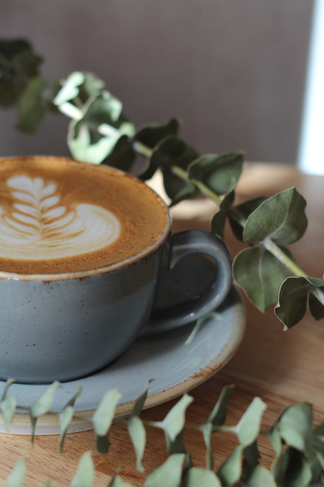 Большая чашка кофе с рисунком на пене на столе с веткой