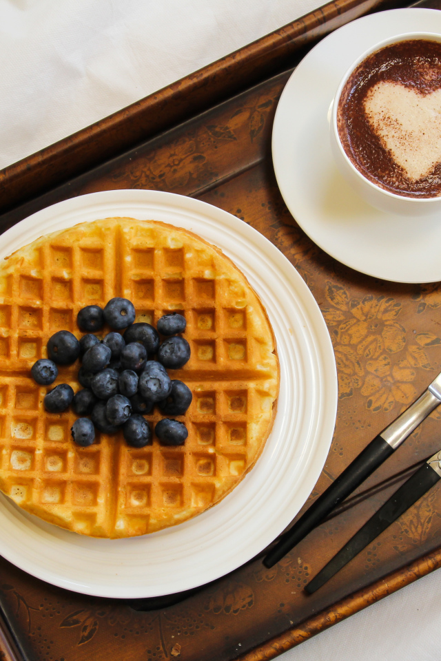 Капучино в чашке на подносе с вафлями и черникой 