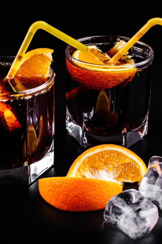 Коктейль с кусочками апельсина на черном фоне со льдом