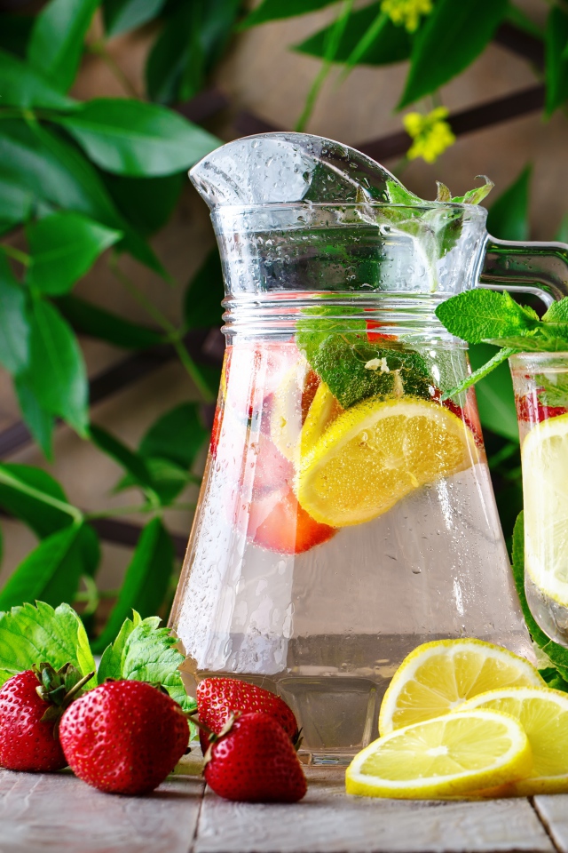 Холодный мохито в графине на столе с клубникой и лимоном