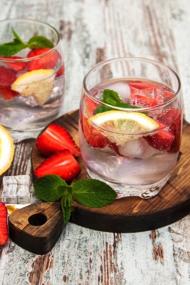 Холодный мохито на столе с ягодами клубники, лимоном и мятой