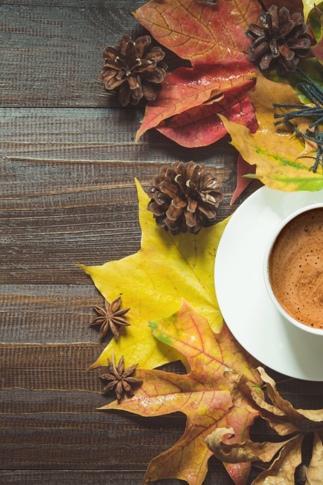 Чашка кофе на столе с шарфом, желтыми листьями и шишками