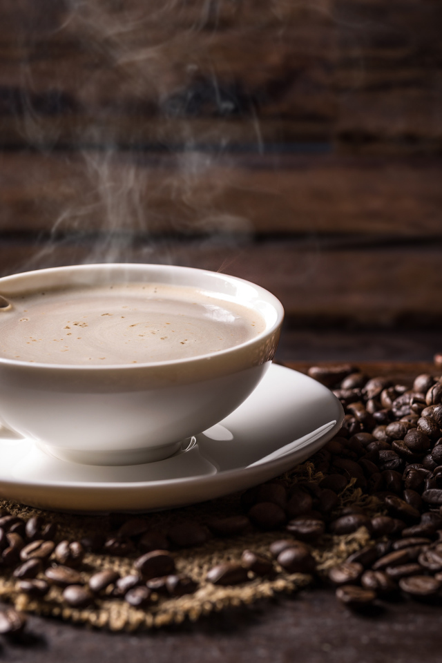 Чашка горячего ароматного кофе на столе с зернами