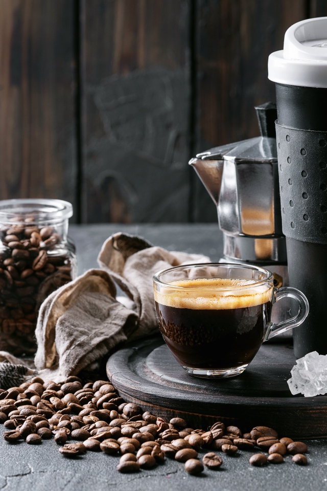 Стеклянная чашка кофе на столе с термосом и зернами
