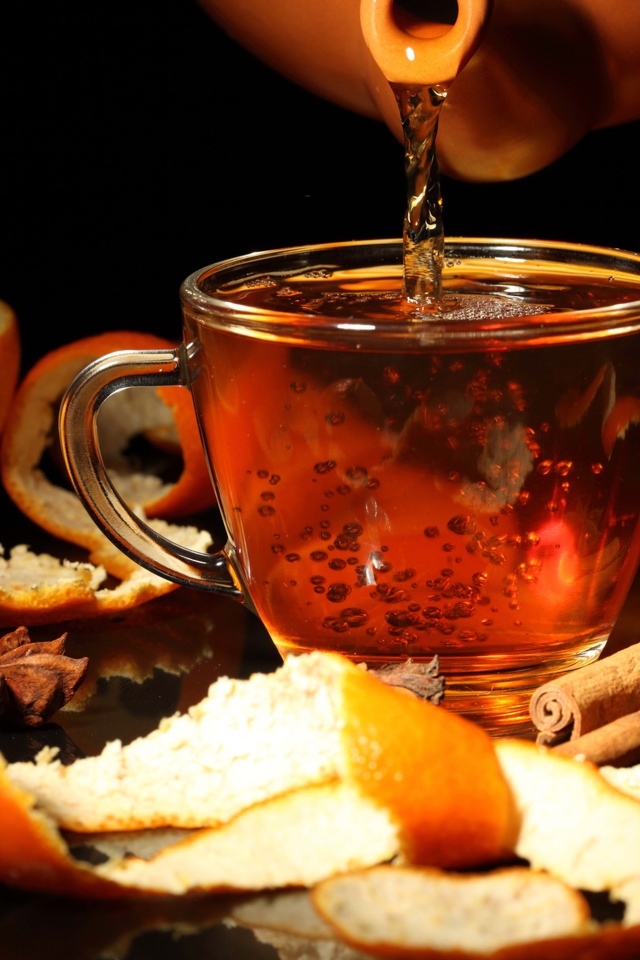 Стеклянная чашка с чаем на столе с апельсинами и корицей